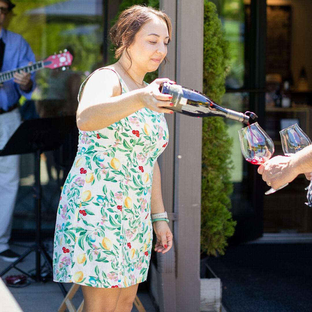 Sydney McMurry pouring a glass of red for guests outside in the sunshine